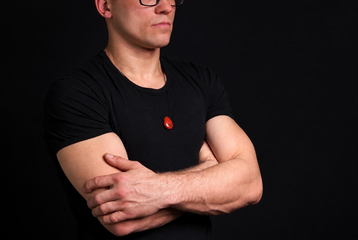 A man in a black t-shirt wears a necklace with a smooth, red drop-shaped pendant against a dark background.