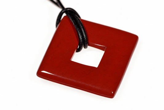 A glossy red square pendant with a central hole, attached to a black cord against a white background.