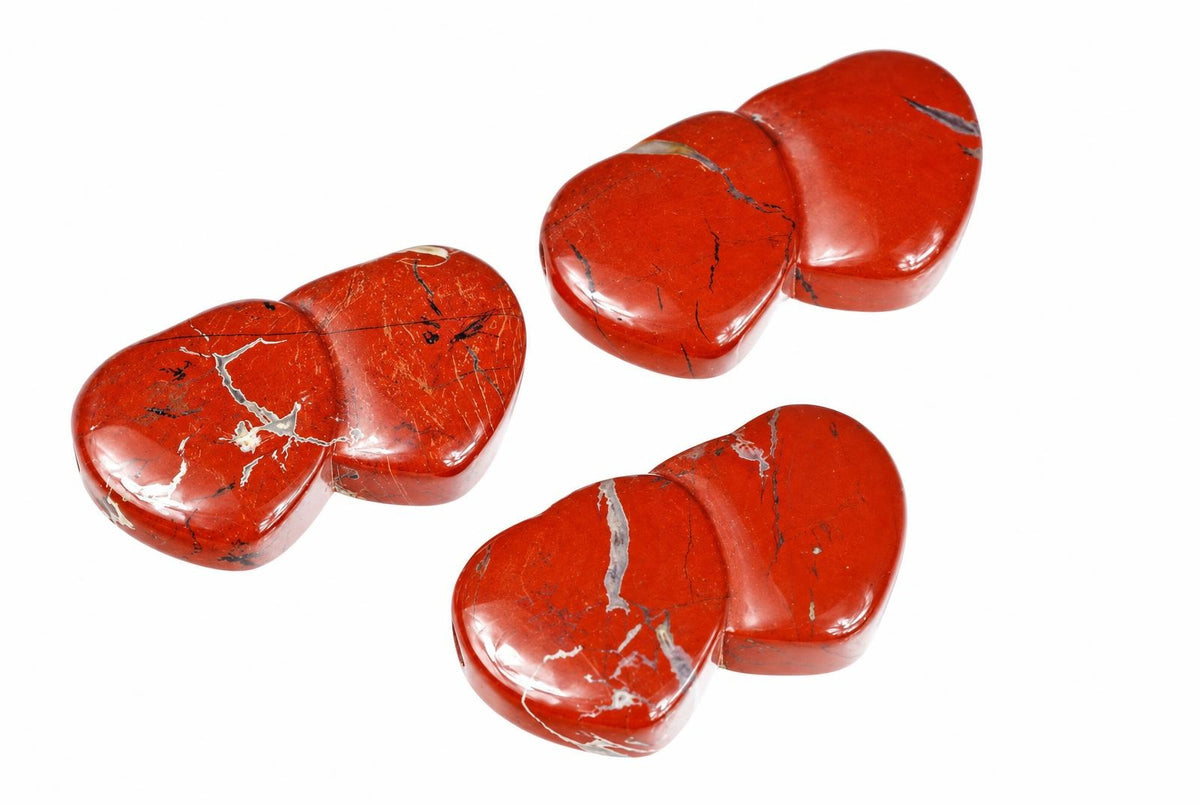 Three polished red jasper pendants shaped like two joined hearts, with white and black veins, on a white background.