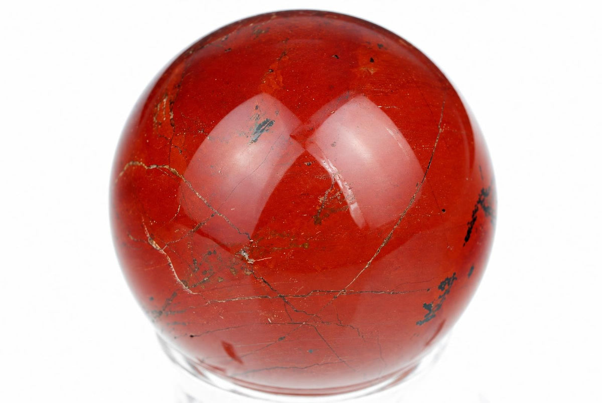 A polished red jasper sphere with visible dark veins and inclusions, resting on a clear stand against a white background.