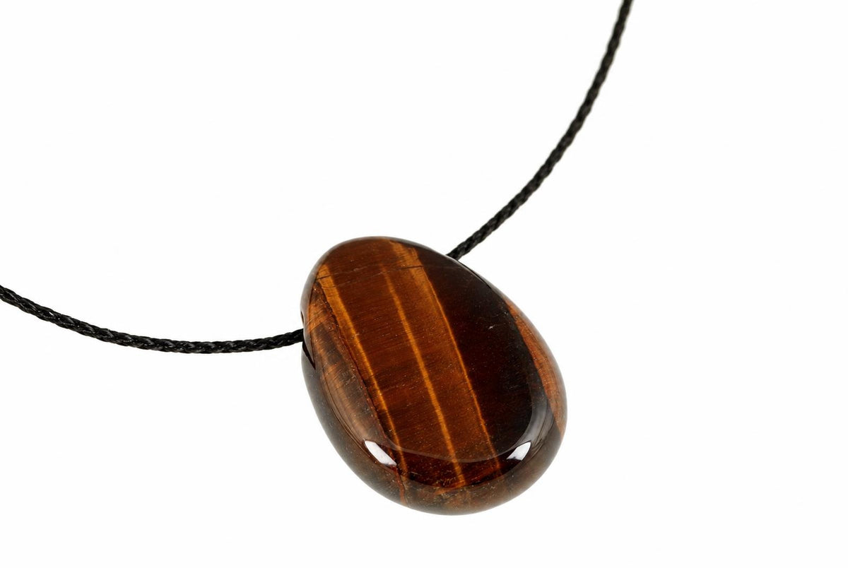 A polished red tiger eye drop pendant shows warm brown tones and bright lengthwise bands, suspended from a black cord on white.