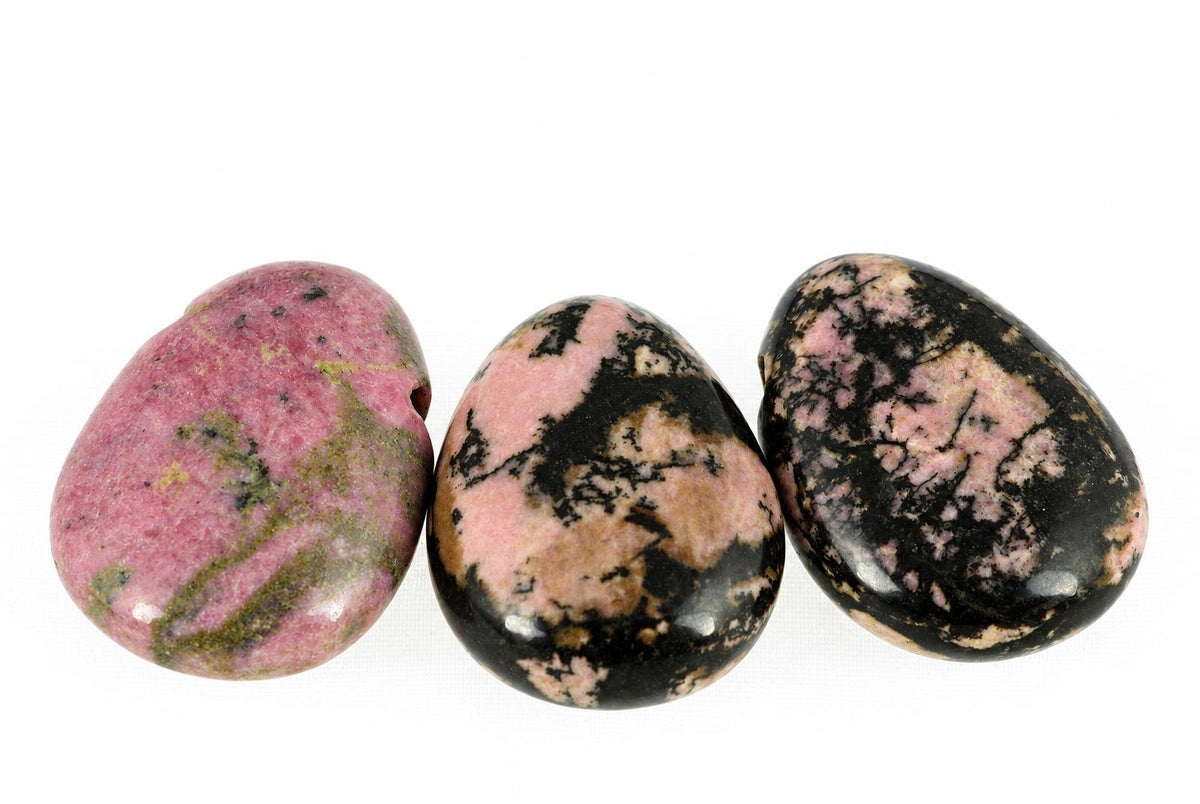 Three polished rhodonite beads with pink, black and green patterns on a white surface.