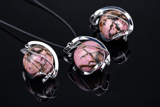 Three Rhodonite pendant spheres with black veining, set in silver-toned metal frames on a dark reflective surface.