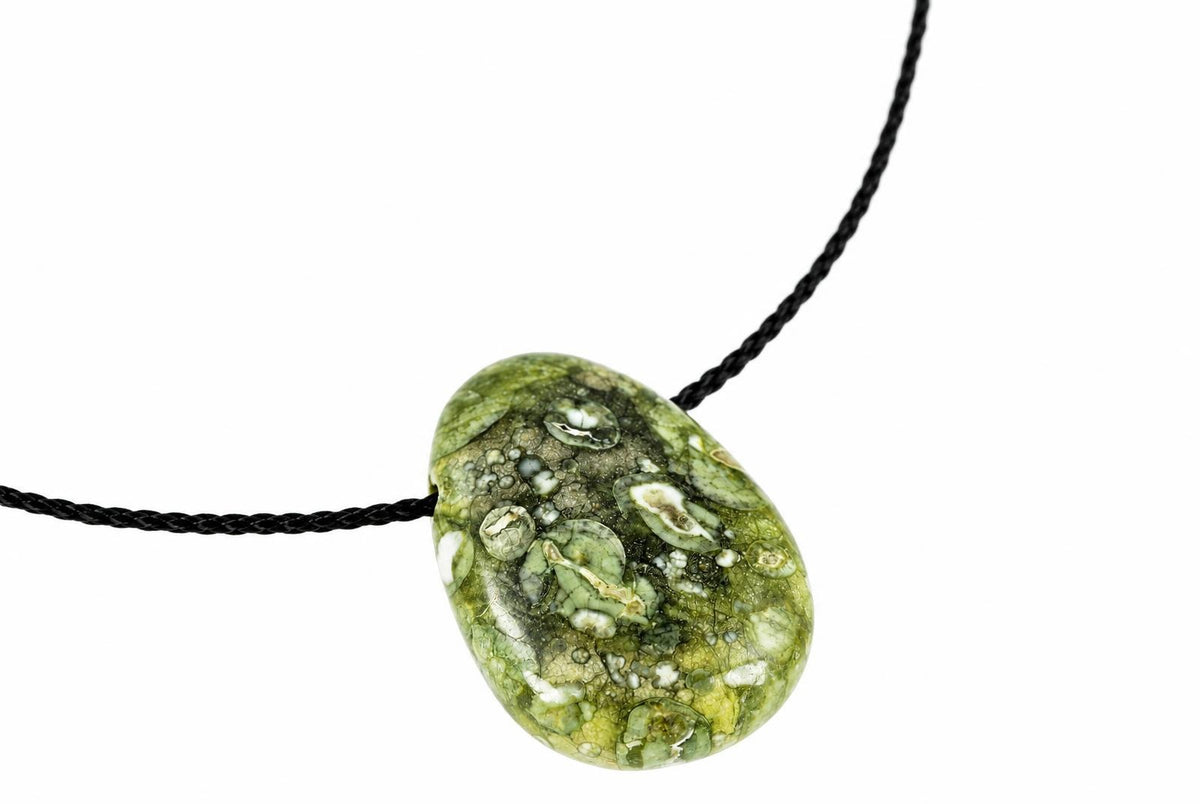 A polished green rhyolite pendant with white and dark inclusions hangs on a black cord against a white background.