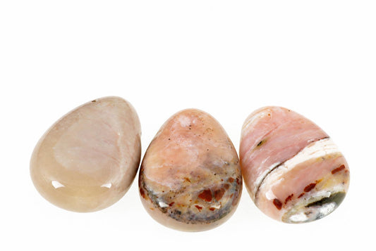 Three polished, teardrop-shaped stones in beige, pink and brown tones arranged on a white surface.