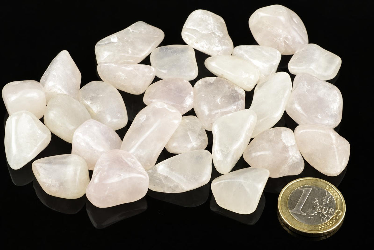 A pile of polished, translucent white to pale pink stones on a dark surface with a one euro coin for scale.