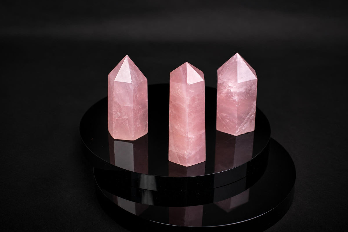 Three pink rose quartz crystal points stand on a dark, reflective circular surface against a black background.