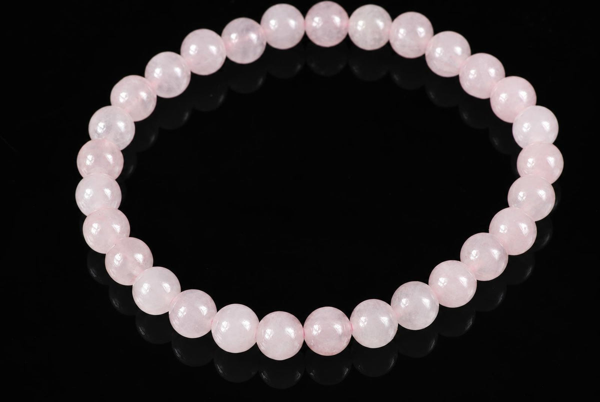 A bracelet of round, pale pink beads arranged in a circle on a dark surface.