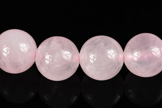 Four round, pale pink beads with a smooth surface and faint internal patterns rest on a dark reflective surface.