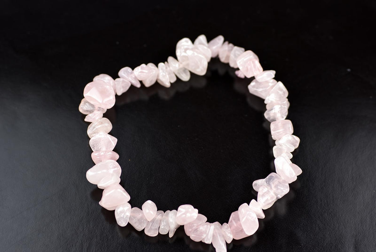 A bracelet made of irregular pink rose quartz chips arranged in a circle on a dark surface.