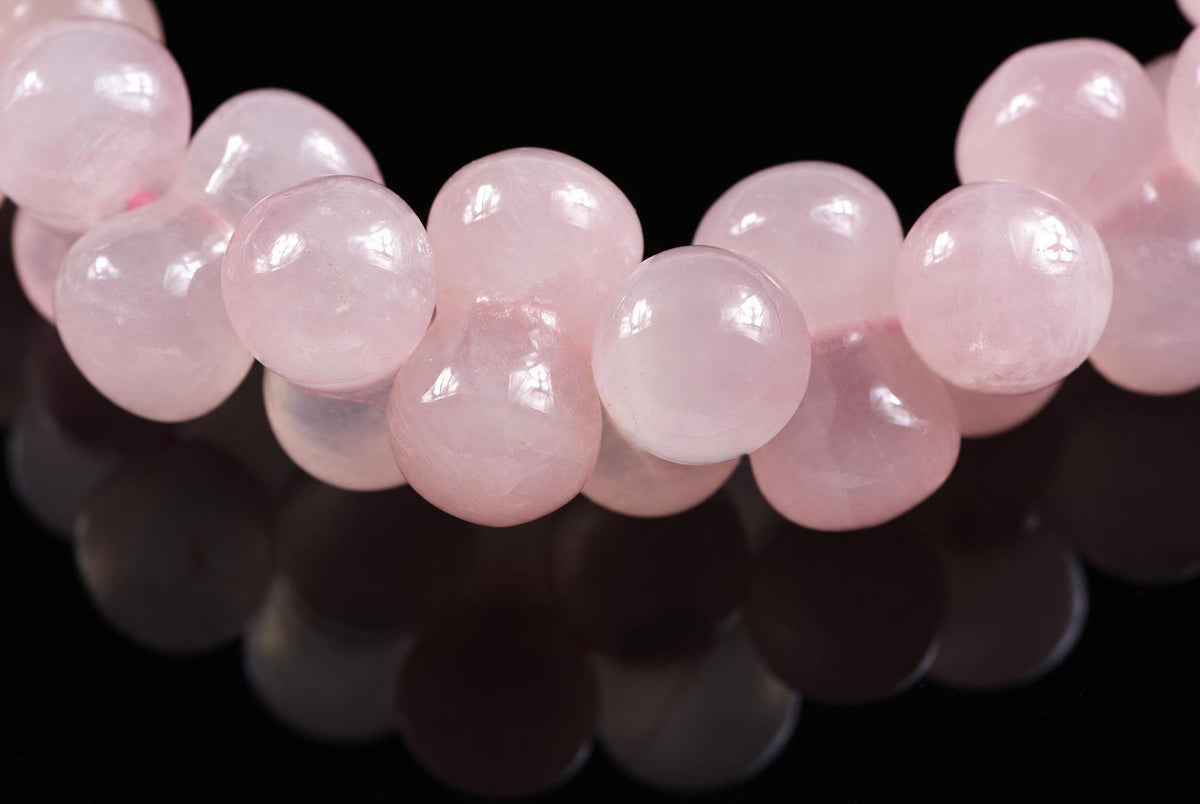 A strand of smooth, round pink beads on a dark surface with reflections.