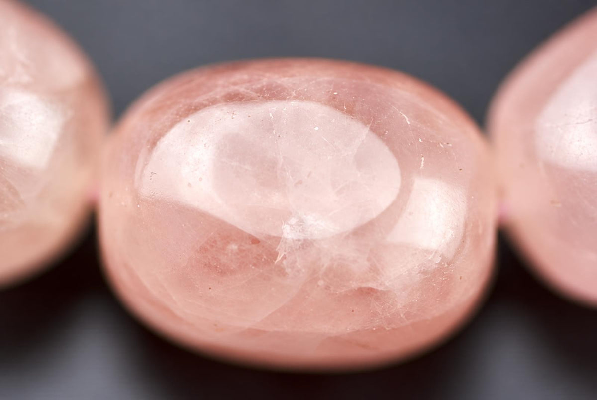 A close-up of a smooth, oval-shaped pink stone bead with a glossy surface and subtle internal patterns.