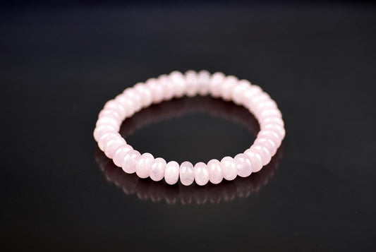 A bracelet of round, pale pink beads arranged in a circle on a dark surface.