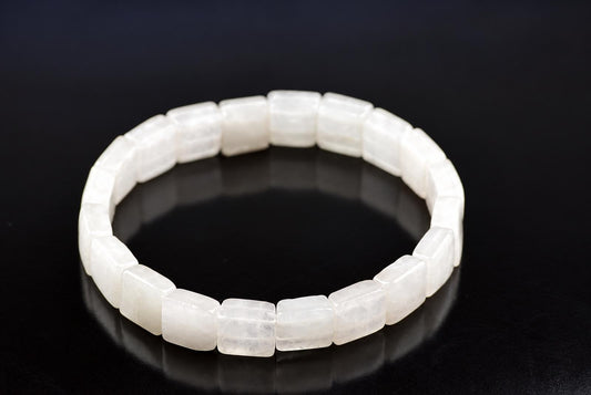 A white square-bead bracelet made of translucent stones rests on a dark surface.