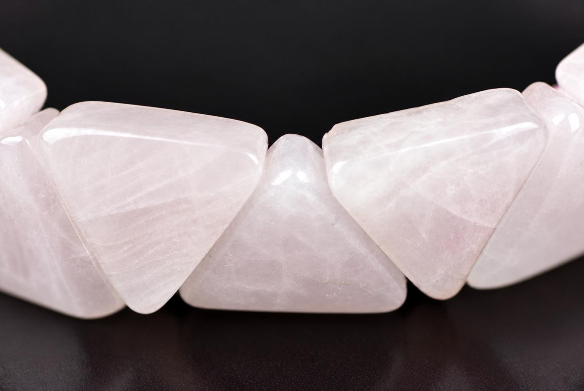 A close-up of a rose quartz bracelet with triangular beads on a dark surface.