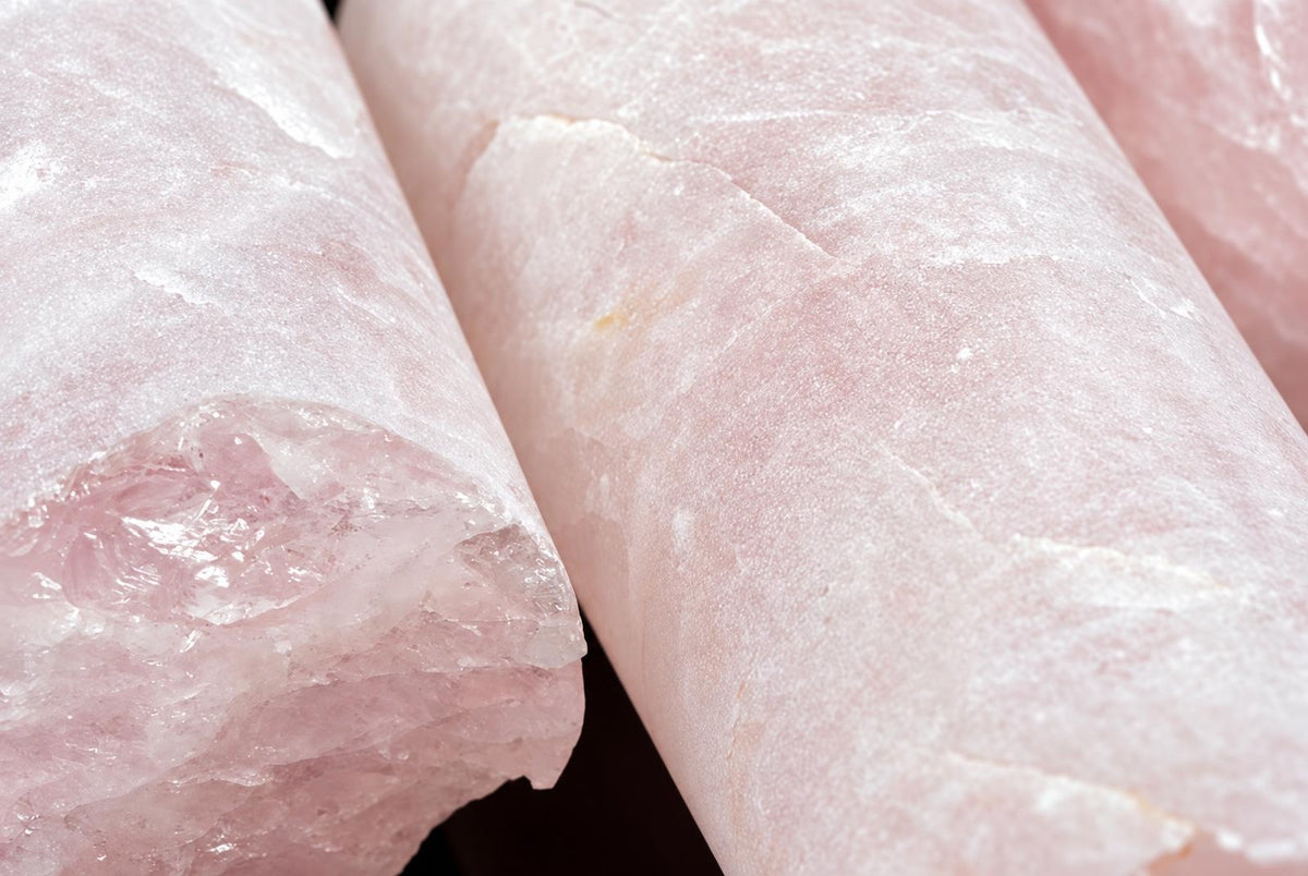 Three polished rose quartz drill cylinders on a dark surface, showing pink crystal texture and smooth edges.
