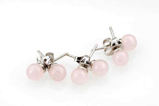 A pair of stud earrings with round, pale pink stones and silver-toned posts on a white surface.