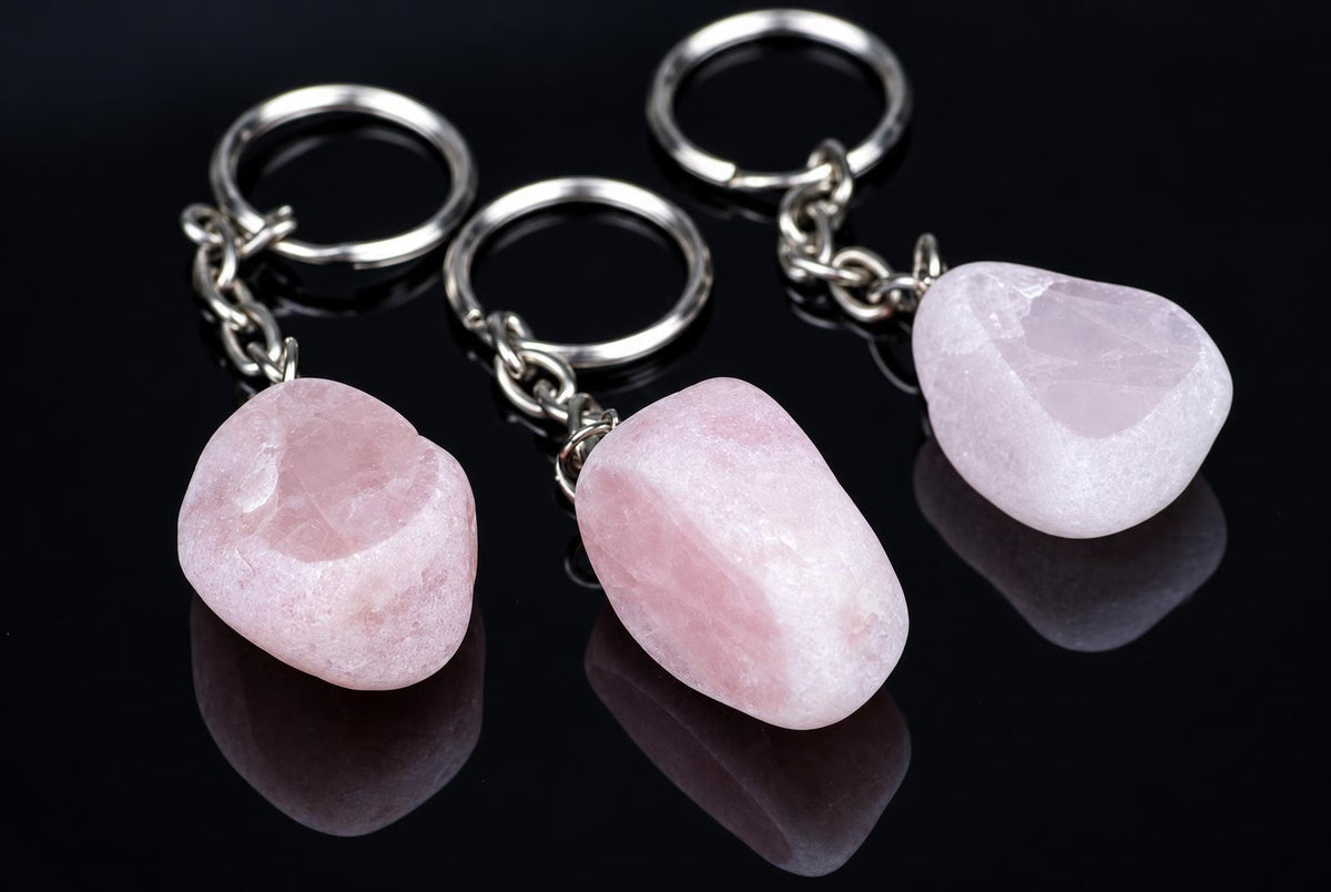 Three rose quartz keychains with silver-toned rings and chains on a dark reflective surface.
