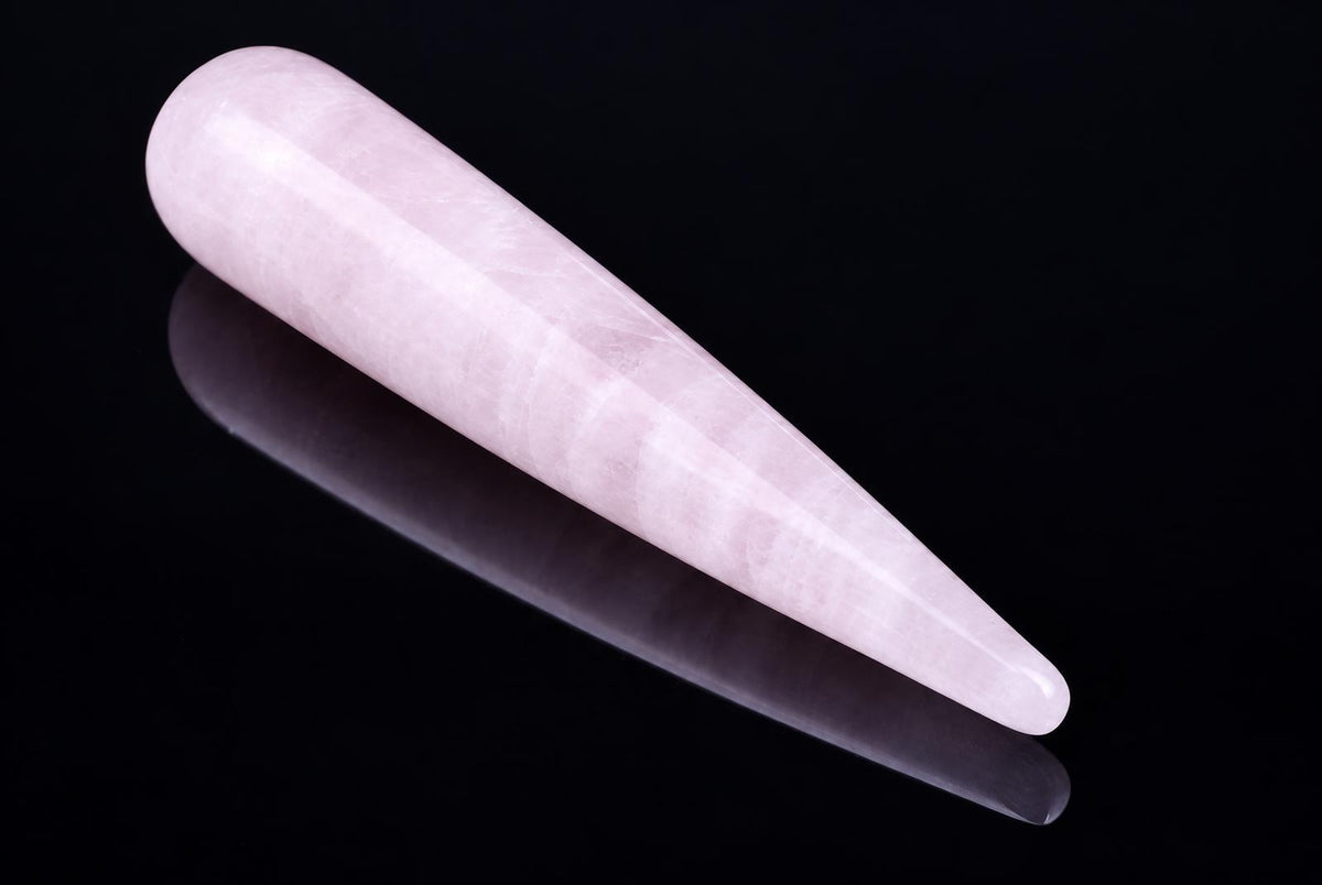 A pale pink, tapered massage stick with a rounded end rests on a dark surface.