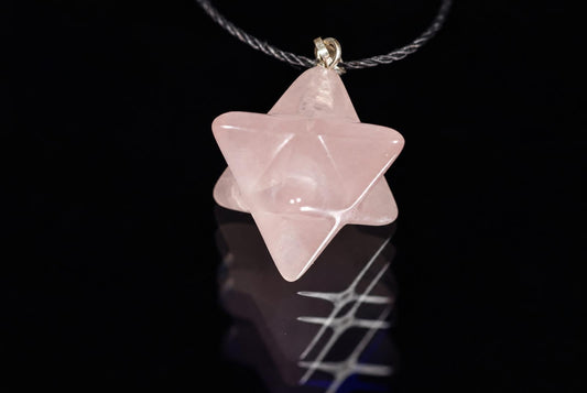 A pink star-shaped pendant hangs from a dark cord against a black background, resting on a reflective surface.