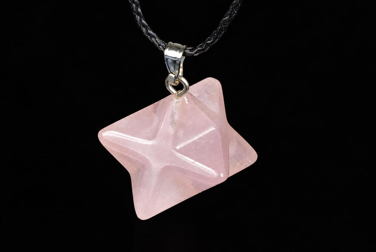 A pink star-shaped pendant with a silver-toned bail hangs from a dark braided cord against a black background.