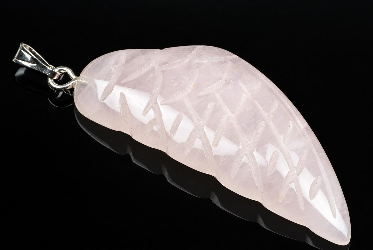 A pale pink carved pendant shaped like a wing, with incised lines on a dark surface.