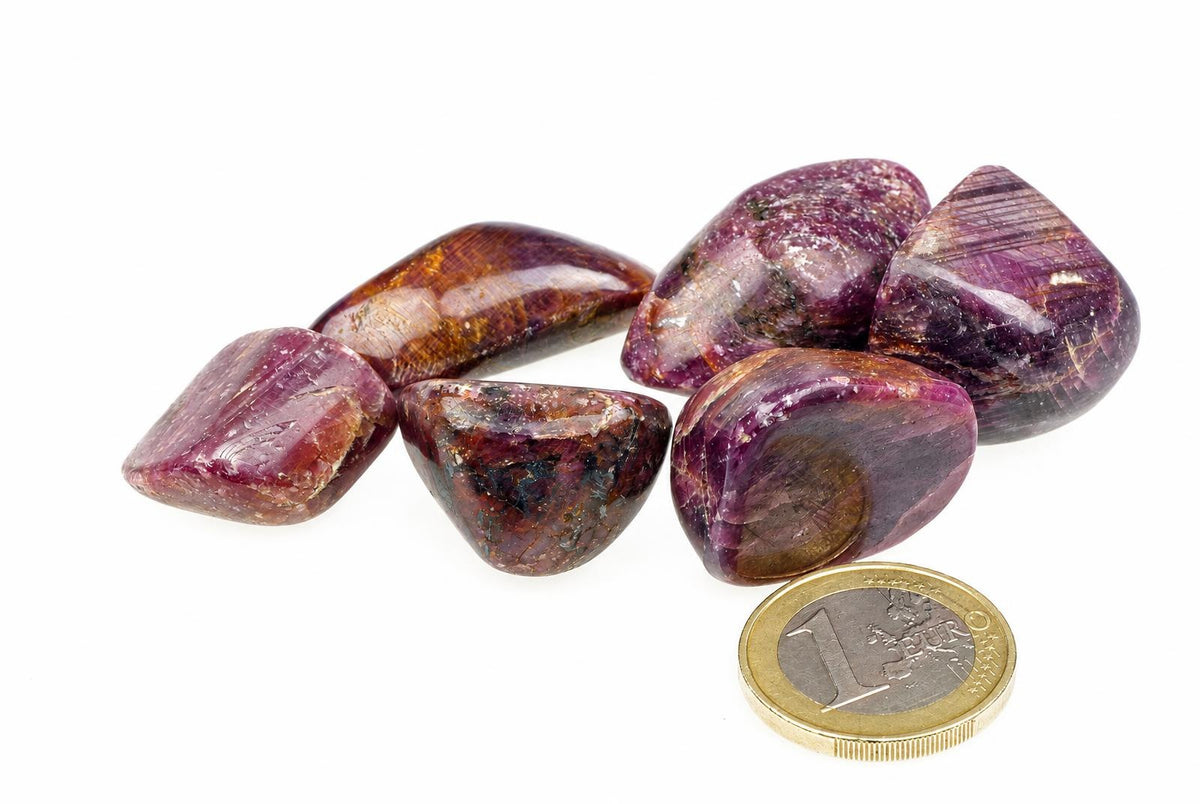 Six polished stones with purple and brown tones on a white surface, next to a one-euro coin.