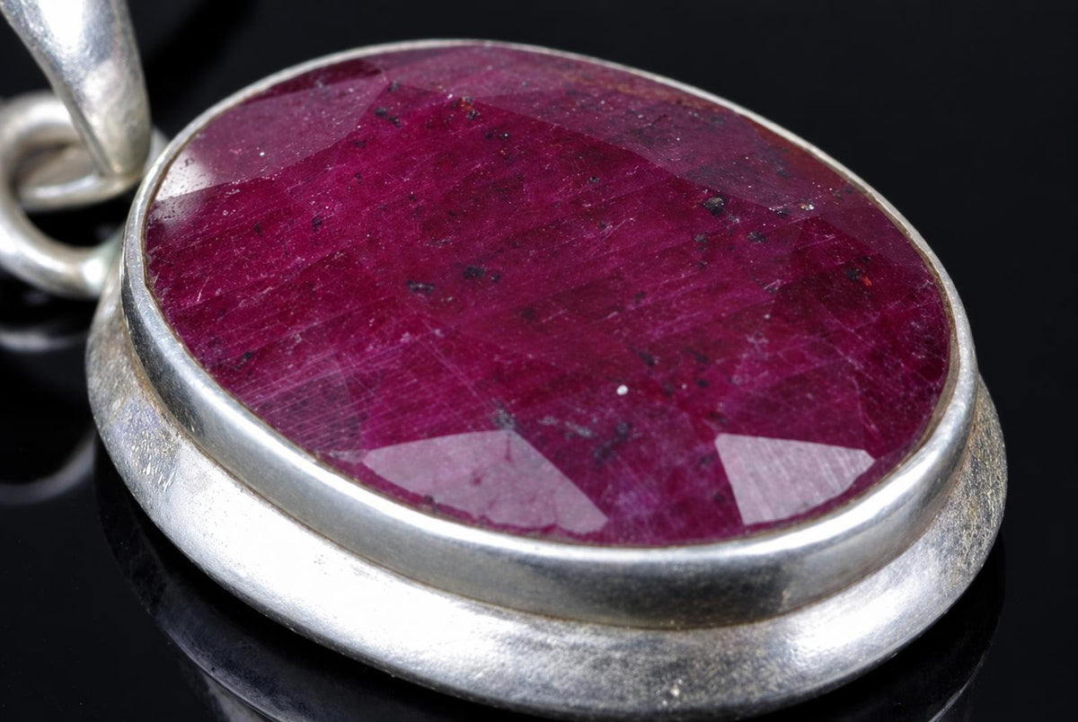 A silver-toned pendant with a large, oval, deep red stone set in a thick bezel on a dark surface.