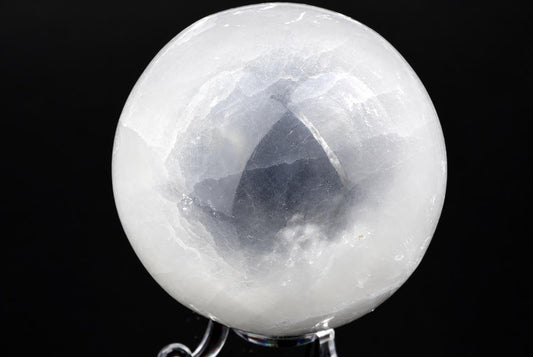 A polished, translucent white sphere with internal cracks and a dark reflection sits on a clear stand against a black background.