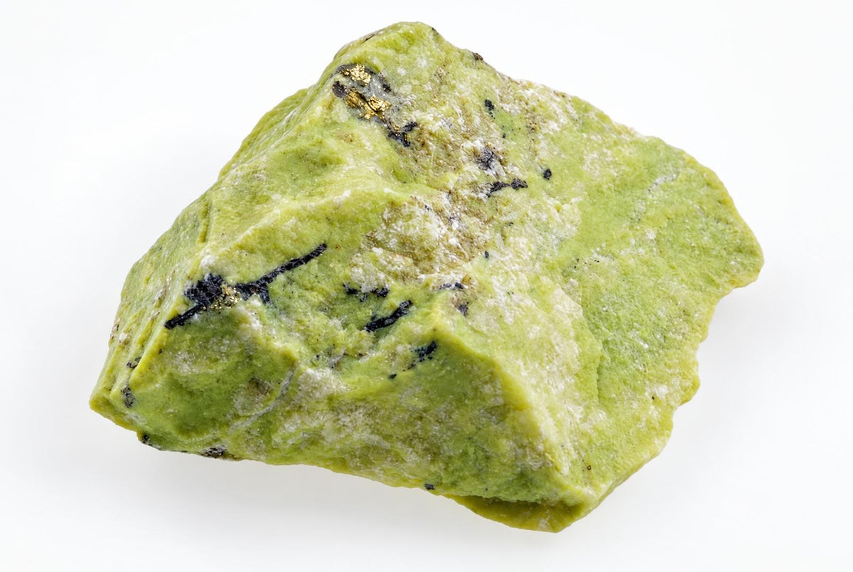 A rough yellowish green serpentinite stone with dark markings and an uneven angular surface is shown against a plain white background.