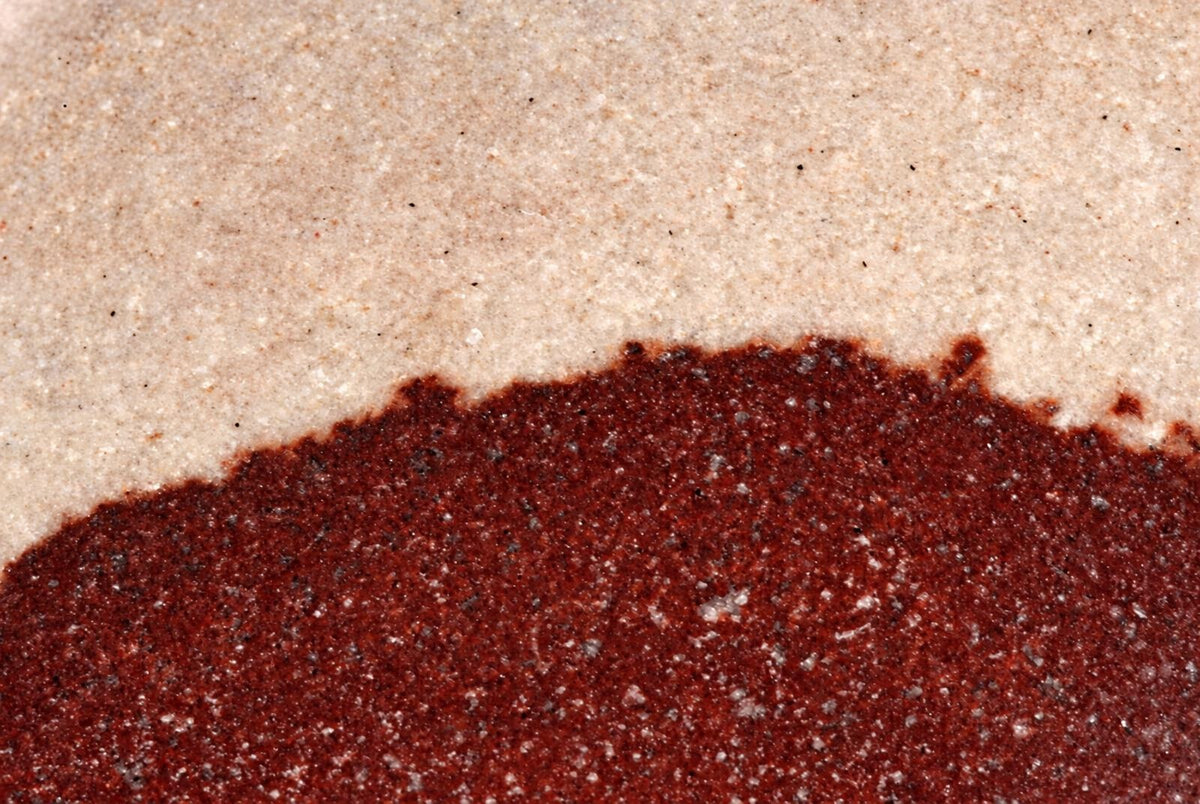 A close-up of a polished stone surface with a dark red lower section and a pale beige upper section.