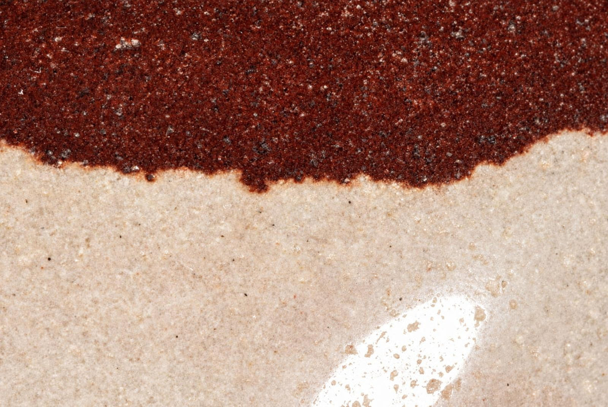 A polished stone object with a dark red-brown top section and a pale beige bottom section on a light surface.