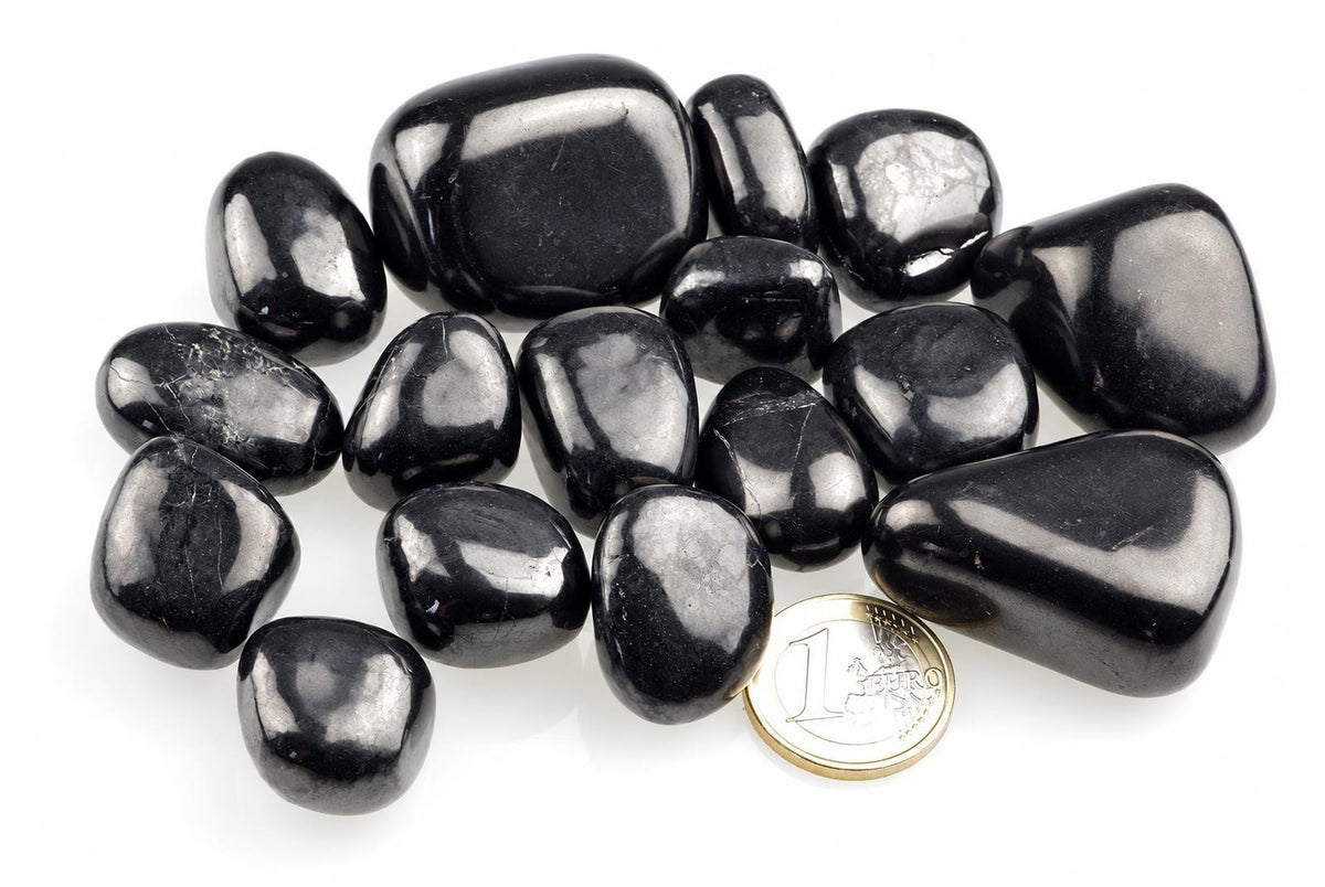 Smooth rounded black stones with bright reflections rest on a white background beside a euro coin.