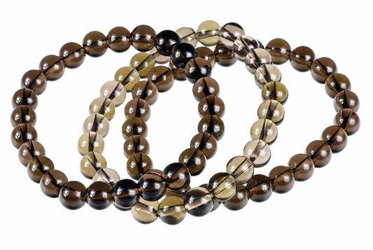 A bracelet of round, polished beads in dark brown, black and pale yellow smoke quartz on a white surface.
