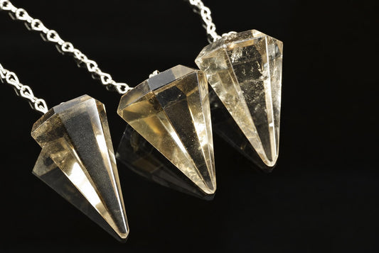 Three silver-toned chains hold faceted, translucent yellow-brown crystal pendants on a dark reflective surface.