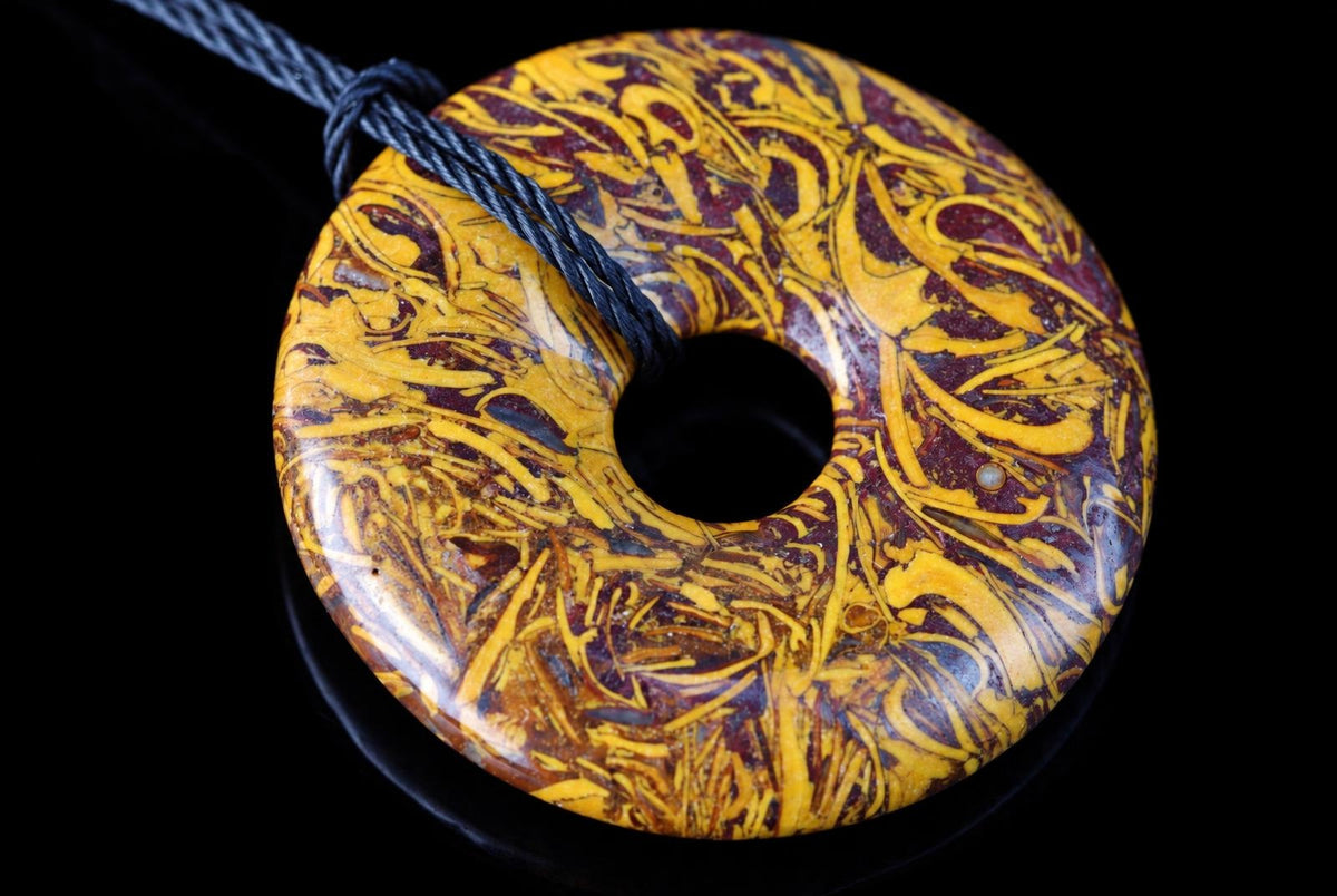 A polished, donut-shaped pendant with swirling yellow and dark red patterns on a black surface.