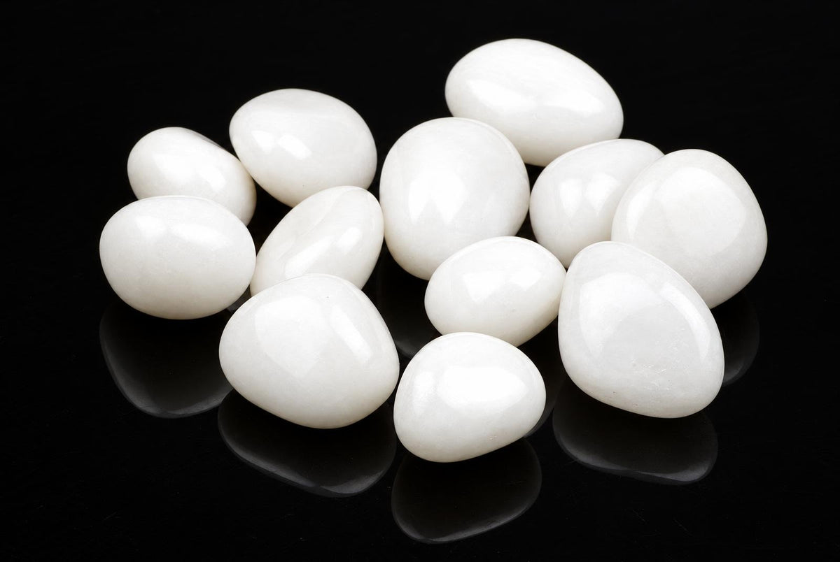 A group of smooth, white quartz stones arranged on a dark reflective surface.