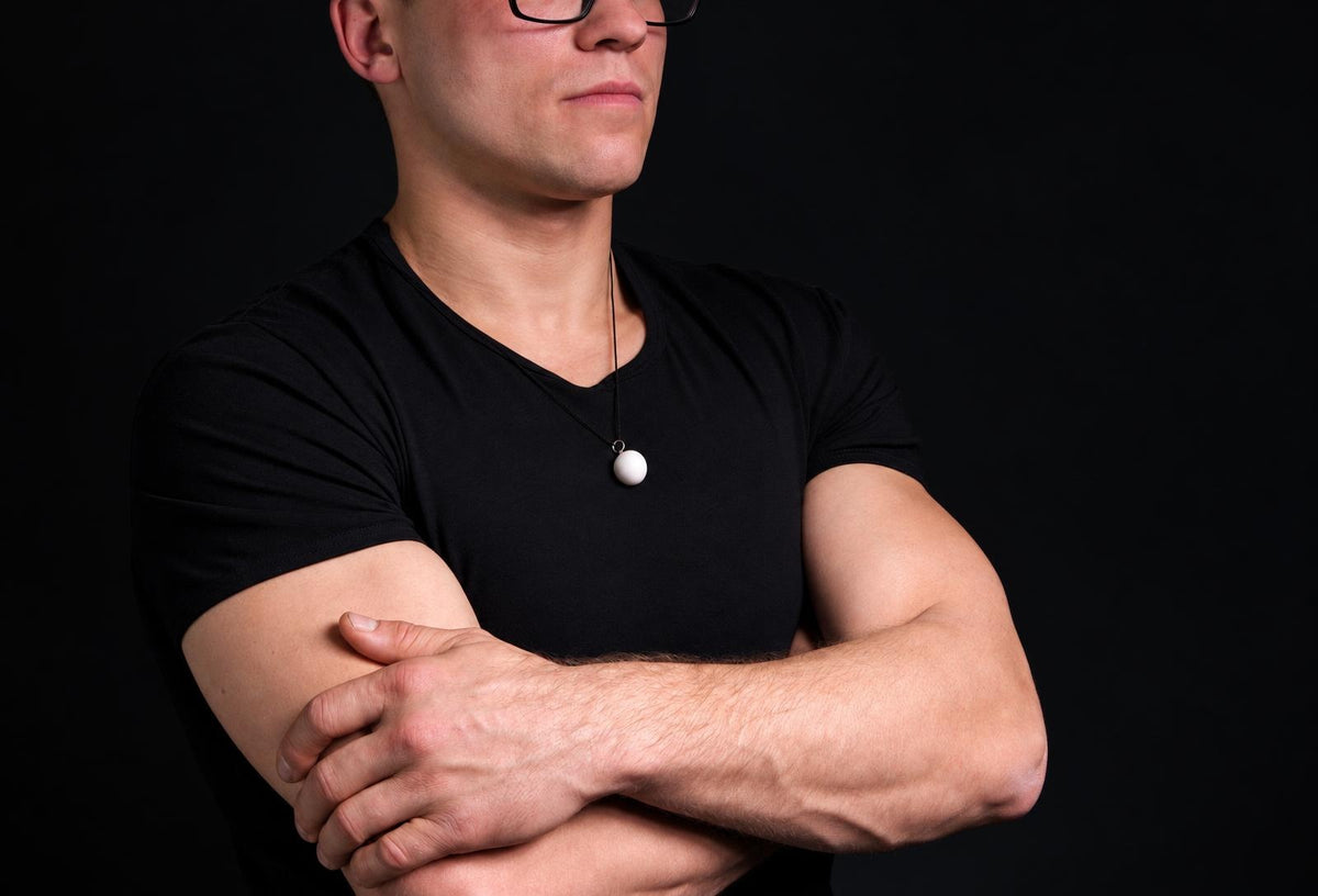 A man in a black t-shirt wears a necklace with a white spherical pendant on a dark surface.