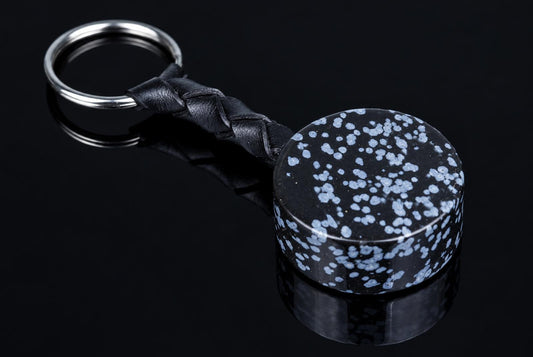 A keychain with a braided black leather strap and a round, dark pendant speckled with light blue spots on a reflective surface.