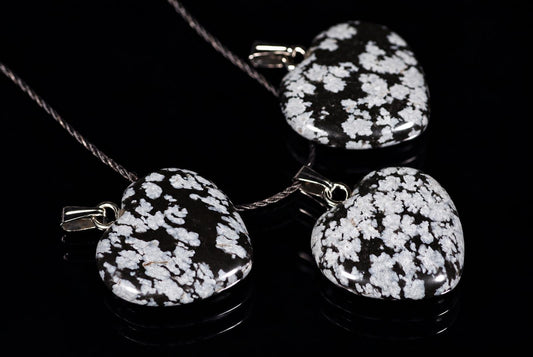 Three heart-shaped pendants with black and white speckled stones on silver-toned cords, resting on a dark reflective surface.