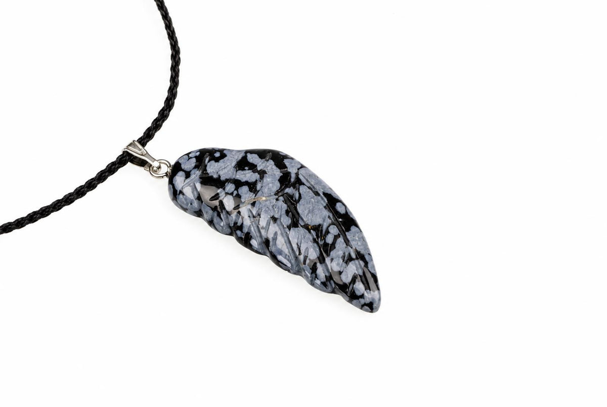 A wing-shaped snowflake obsidian pendant with pale grey speckles and a silver-tone loop hangs from a black cord against white.