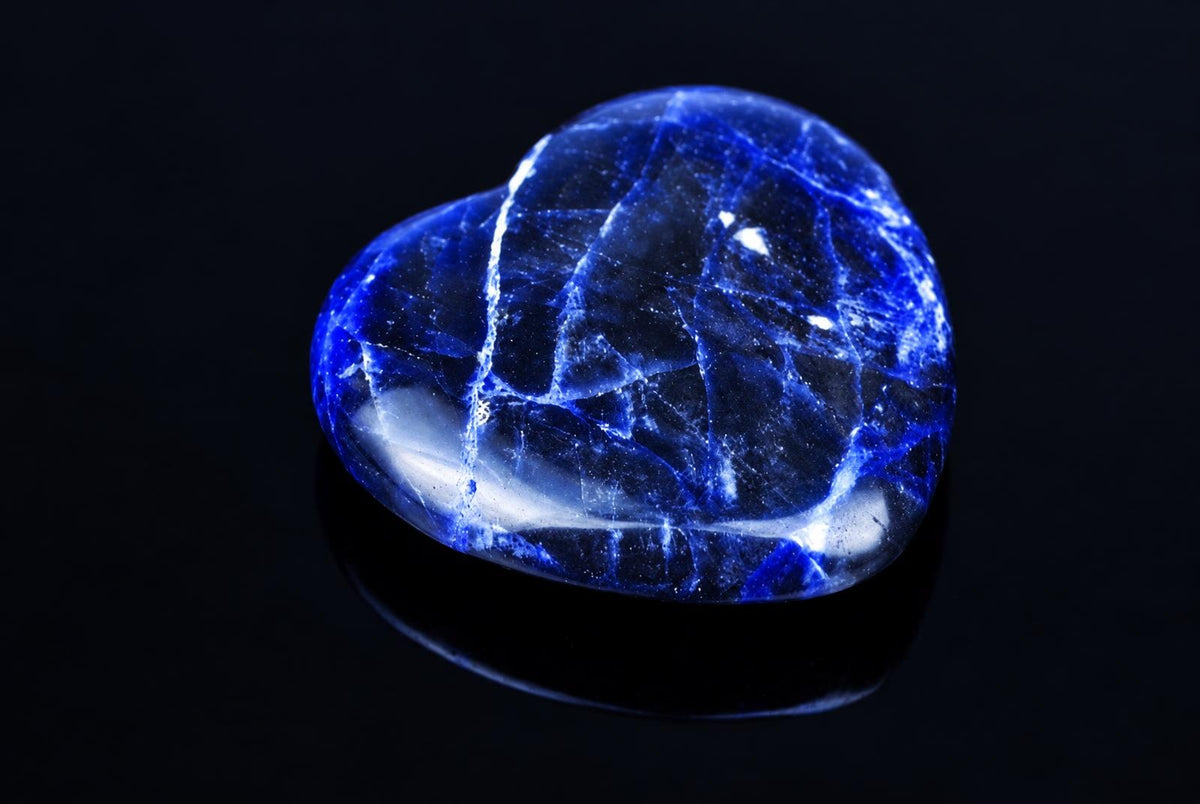 A polished sodalite stone shaped like a heart, featuring deep blue and white veining on a dark reflective surface.