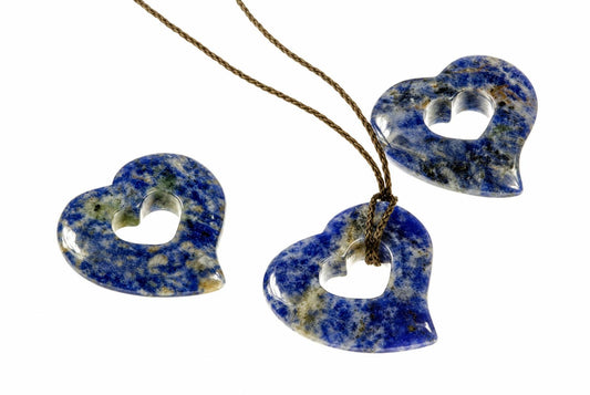 Three blue sodalite heart pendants with a central hole, one on a brown cord against a white background.