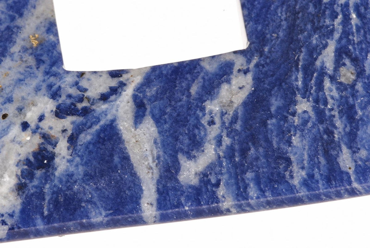 A close-up of a polished sodalite stone with deep blue and white swirling patterns, resting on a pale surface.