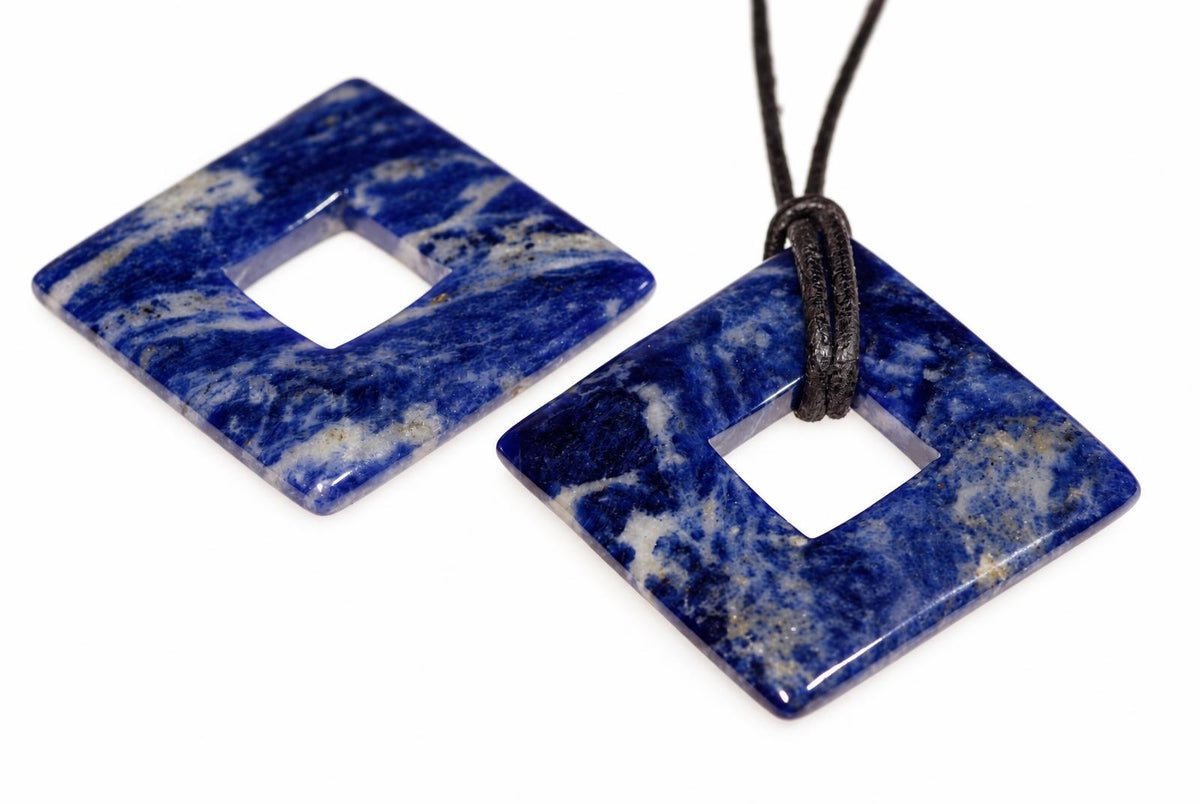 Two square sodalite pendants with a central hole, one on a dark cord, both showing blue and white patterns on a white surface.