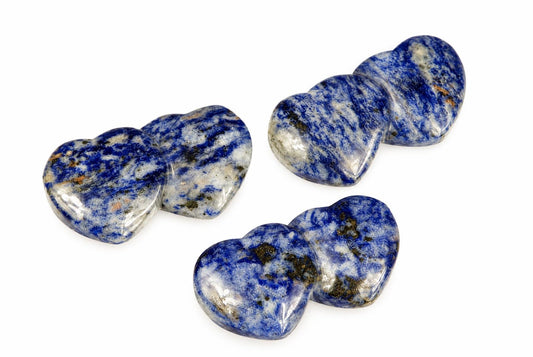 Three polished sodalite heart-shaped pendants with blue, white and dark inclusions on a pale surface.