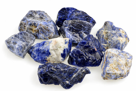 A pile of raw sodalite stones with deep blue and white patterns on a pale surface.