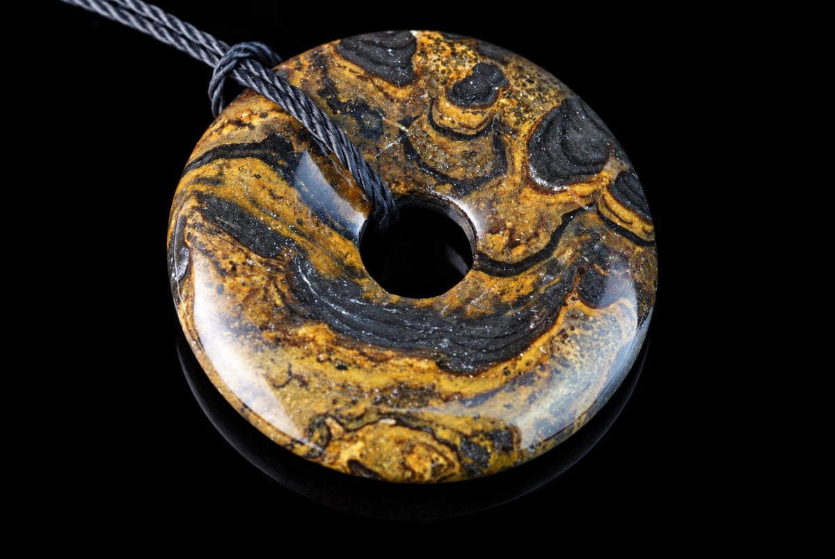 A polished, donut-shaped pendant with swirling black and golden-brown patterns on a dark surface.
