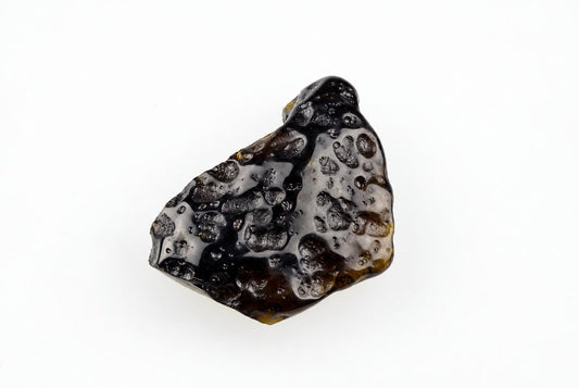 A dark, irregularly shaped tektite with a glossy surface and numerous small bubbles on a white background.