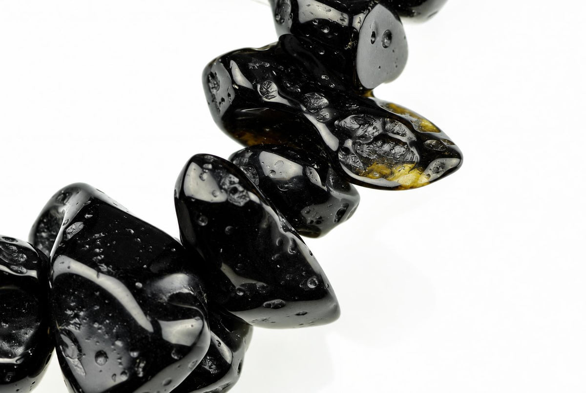 A close-up of a dark, glossy bracelet with irregular beads on a white background.